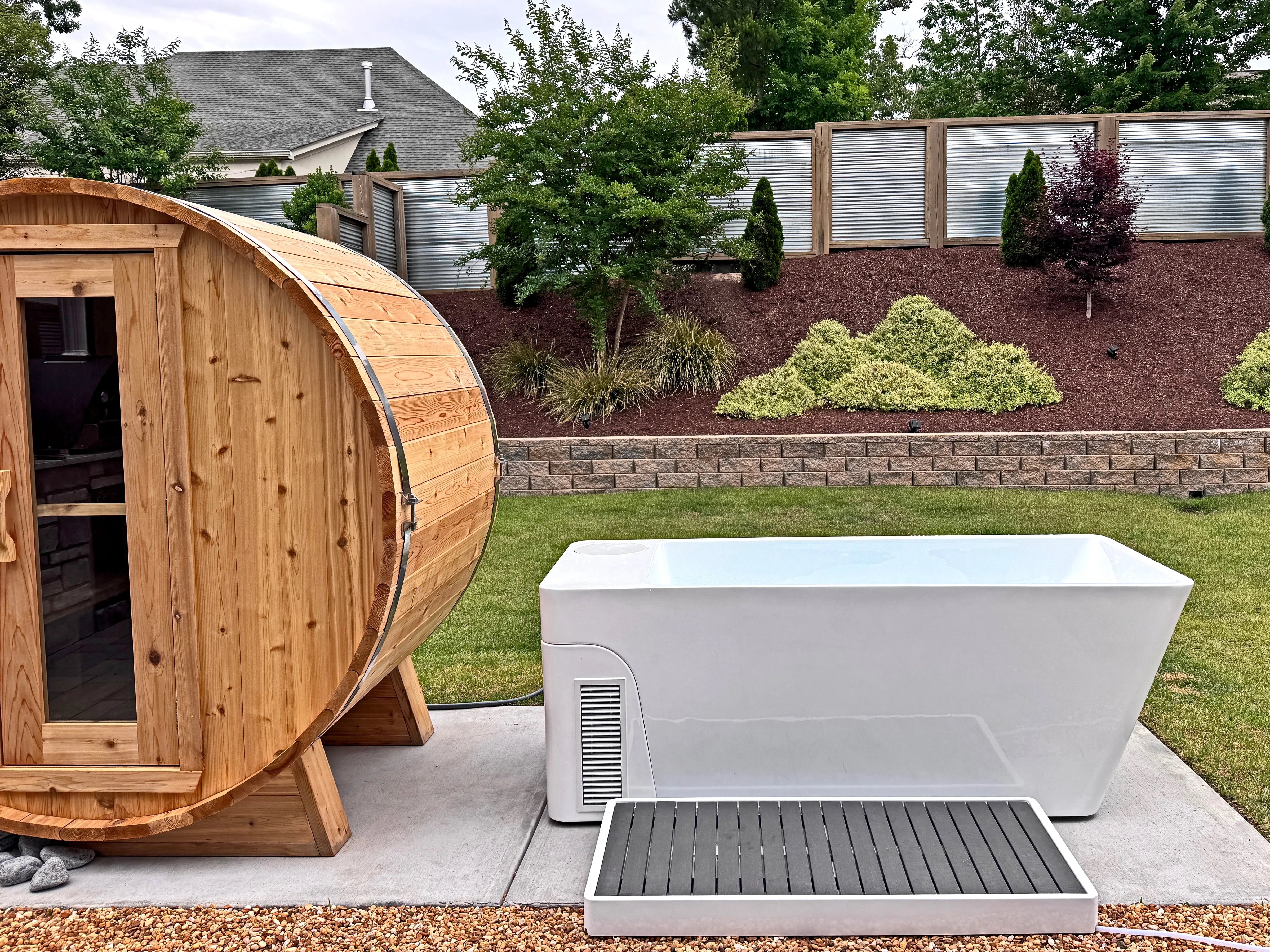 Outdoor home wellness circuit featuring a rustic wooden barrel sauna next to a modern Avanto All-In cold plunge tub for complete contrast therapy and active recovery.